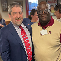 Photo of Dean Samuels at an event with an attendee with a yellow sweater vest on. 