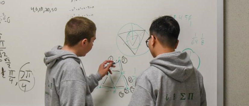 Two boys doing math on a whiteboard.