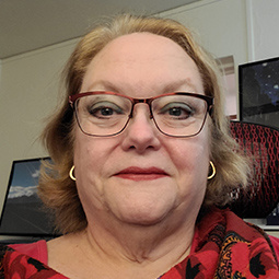 a photo of a woman with blonde hair and redish glasses on smiling indoors