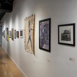Many pieces of student artwork are hung on a white wall.