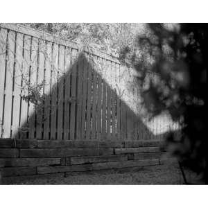A black and white photograph by Joshua Kendrick depicting a triangular shadow on a fence.