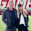 Justin Tupper and his wife, Torrie Wilson, smile for a photo on a football field.