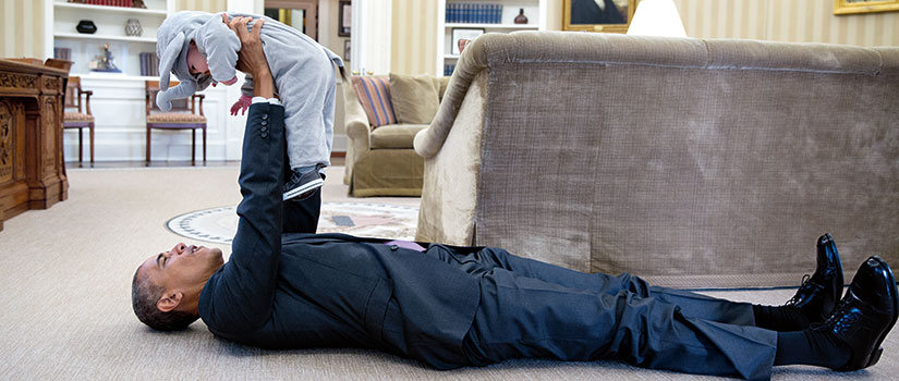 A photo that Pete Souza took of President Obama in the Oval Office. Obama is lying on the floor holding a baby up.