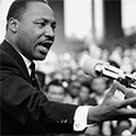 Martin Luther King at a microphone, one hand outstretched
