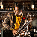 Black man with saxophone sitting in front of a bar