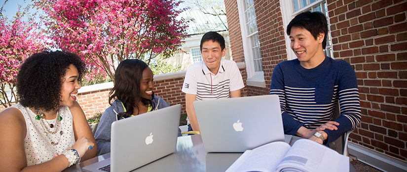 several diverse students sitting outside with computers
