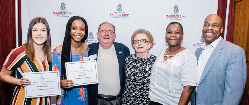 two smiling women hold certificates while four older people stand nearby