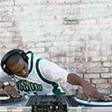 African American man mixing tracks on two turntables in front of white brick wall