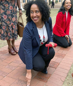 Tjuan Dogan, smiling as she touches the brick path on the historic Horseshoe. other figures are nearby.