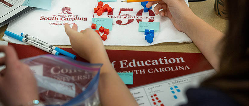 a child's hands hold a pencil amidst USC banners and small colored cubes