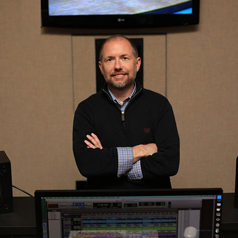 Jeff Francis in his studio standing under a monitor and flanked by speakers