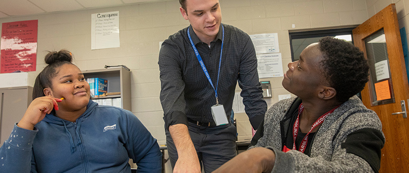 A male teacher points to something off-camera while two students look up at him.