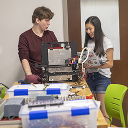 two students talk next to a 3D printer