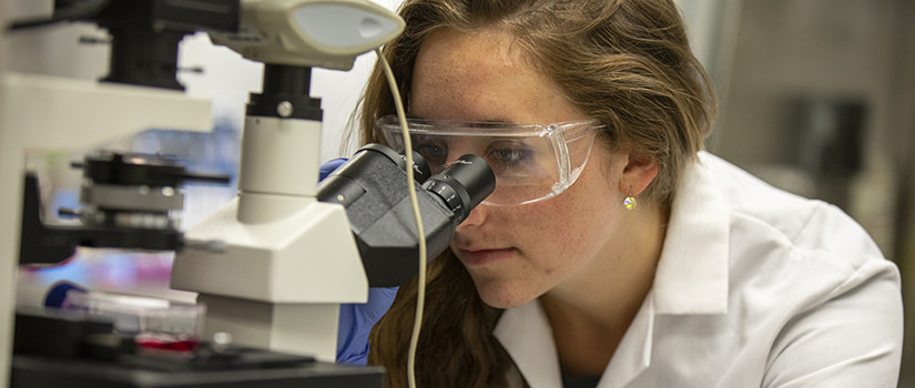 female student looks into microscope