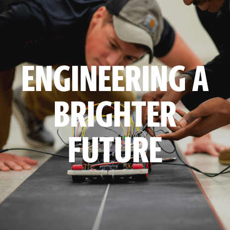 text: engineering a brighter future over a small electric car and two male students