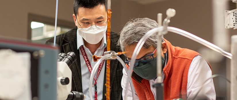 two men working in a lab wearing safety glasses and masks