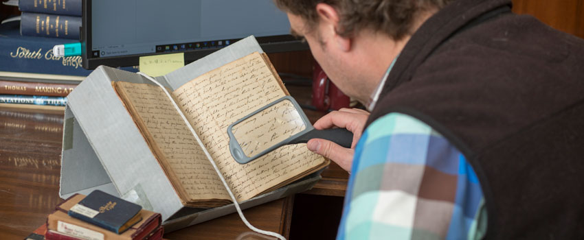 A student looks at an old manuscript using a hand-held magnifying glass.