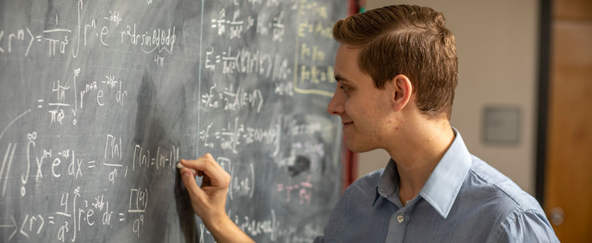 Eric Rohm works an equation on a chalk board.