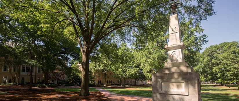 The Maxcy Monument in the historic Horseshoe area of campus, dappled with sun shining through the tree next to it.
