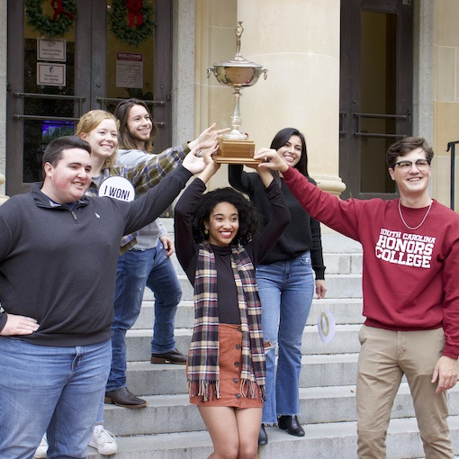 National fellowship winners hold large trophy on the steps of McKissick