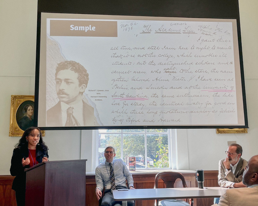 A young black woman presenting behind a podium with a large screen behind her.