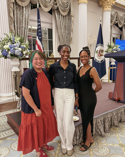 Three women posing at the White House with US flags in the background