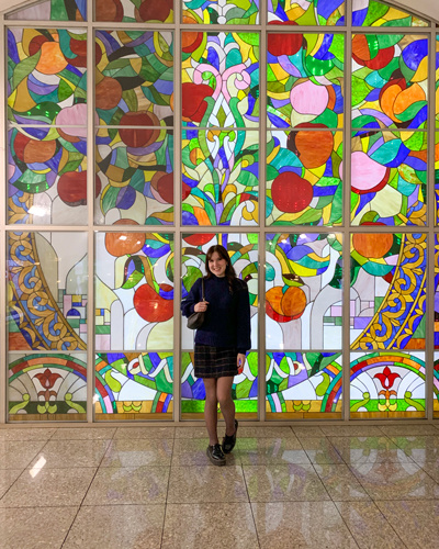 A young woman in front of a stained glass wall