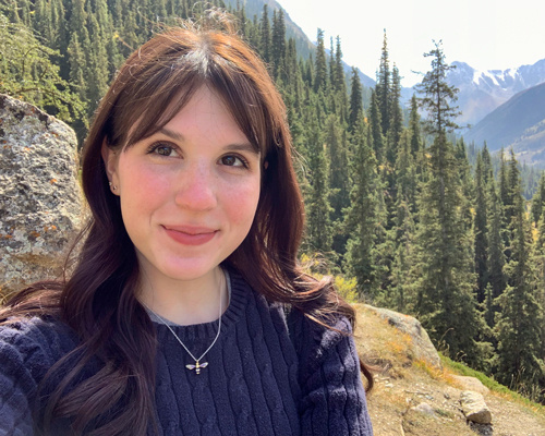 A young woman smiling with a forest and mountains in the background