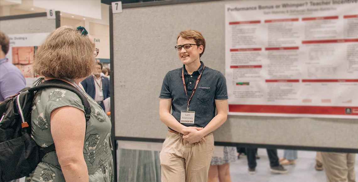 Male student standing in front of poster smiling at a woman