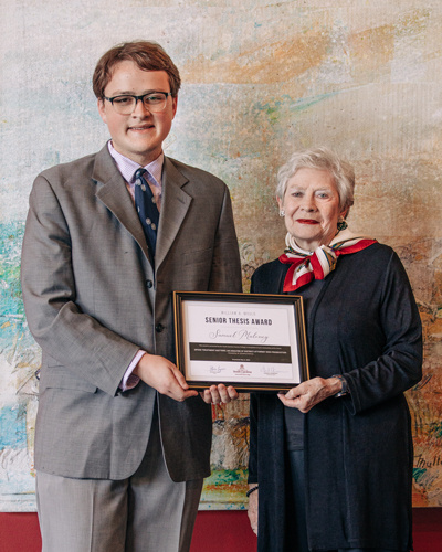 Man in a gray suit holding an award plaque with a woman wearing black.