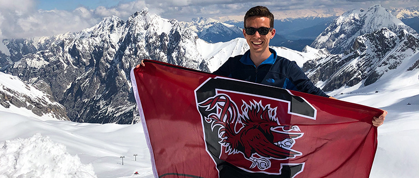 Student holding a UofSC flag on the top of a snow covered mountain.