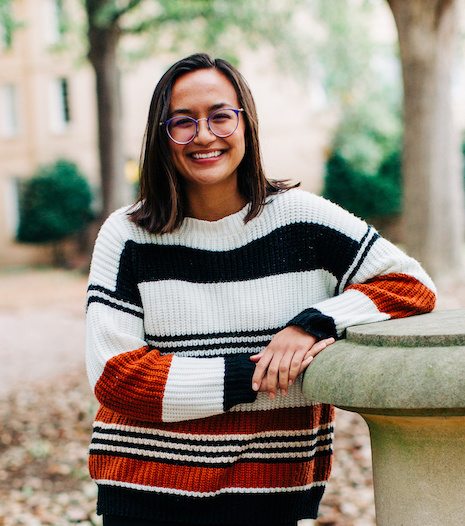 Layne Scopano, Honors student, dark, shoulder length hair with glasses wearing a striped sweater standing on the UofSC Horseshoe