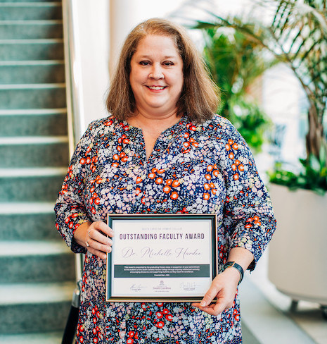 Dr. Michelle Hardee holds award certificate in front of staircase
