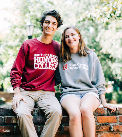 Two students wearing Honors shirts sitting on Horseshoe wall