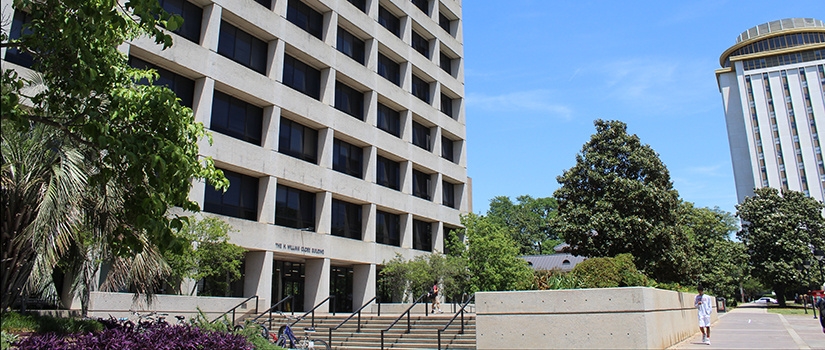 The Close-Hipp building, the home of the College of Hospitality, Retail and Sport Management during a clear sunny day. Close-Hipp is an 8-story building with an outdoor patio area surrounded by garden landscaping. The Capstone building, with a rotating restaurant at its top,  is in the background.