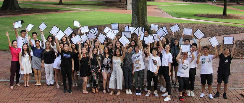 Photo of international students with their certificates held high on the lush green space known as the Horseshoe at the historic heart of the University of South Carolina