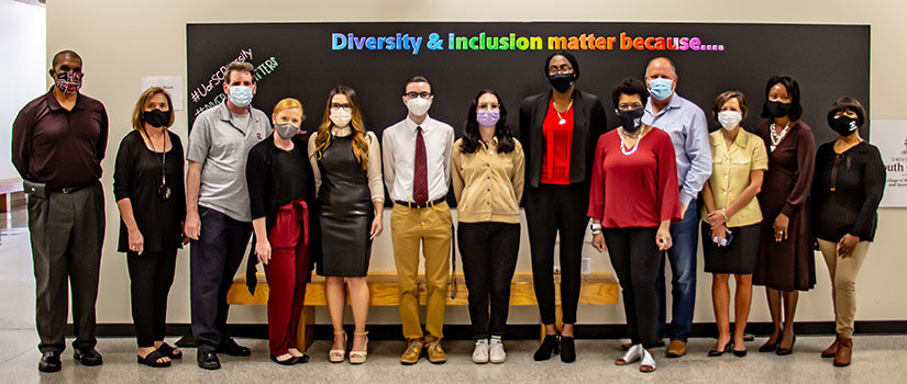 The Diversity and Inclusion Committee stands in front of the diversity and inclusion chalkboard, a public board for students, faculty and staff to share their ideas about why diversity matters.