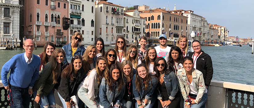 Students stand on the ancient waterfront in Venice with historic villas in the background.