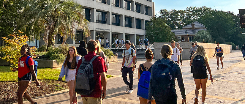 Students walk around outside the USC campus in front of the Close-Hipp building on a sunny day.
