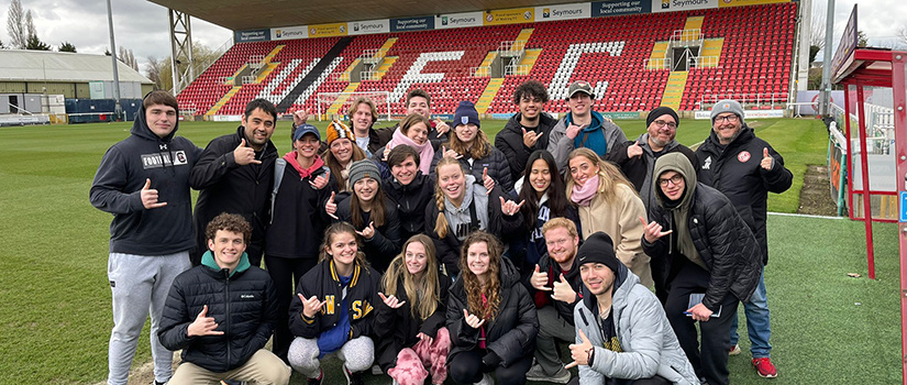 Students attending a study abroad trip over spring break in England throw up the Spurs Up hand sign while visiting a soccer stadium.