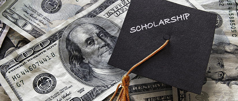 A collection of paper money with a $100 bill prominently featured and a graduation cap on top with the word "scholarship" written on it.
