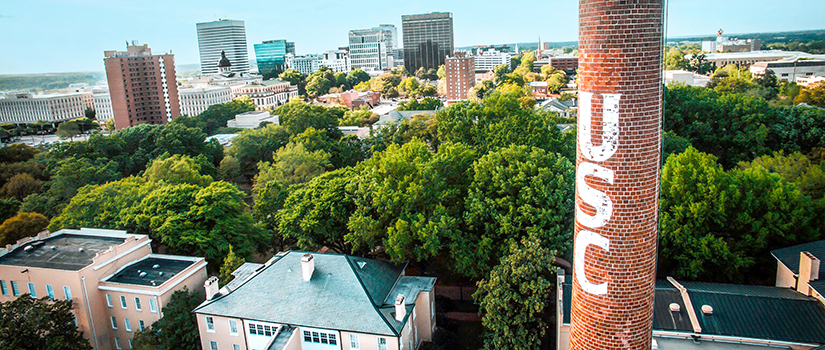 An aerial view of downtown Columbia as seen from the campus with a smokestack in the foreground with the letters USC on it.