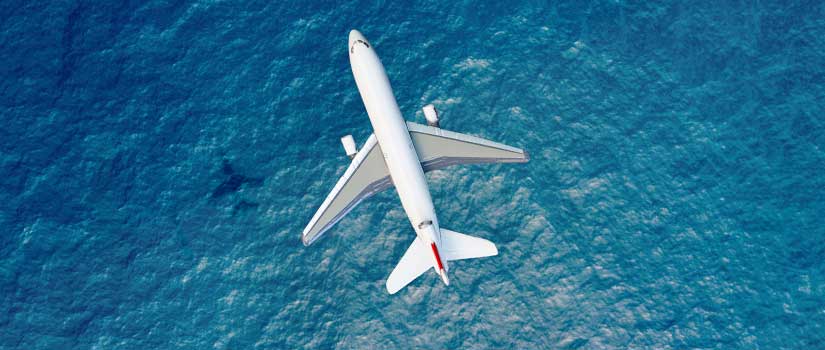 Photograph of an airliner flying over a blue ocean.
