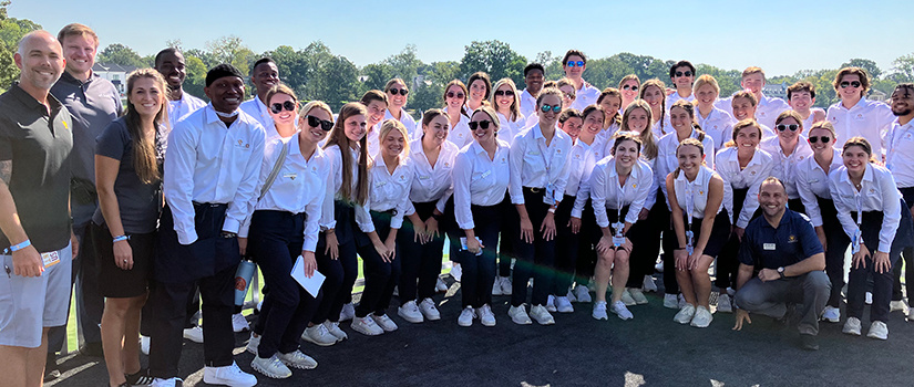 A large group of hospitality, retail and sport management students pose for a photo together at Quail Hollow, host site for the 2022 President's Cup.