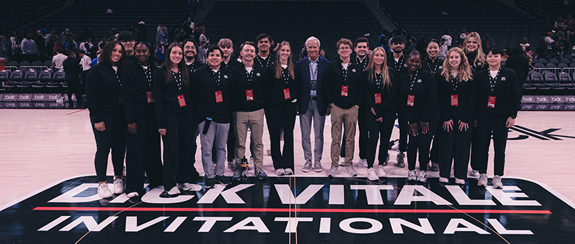 Group of University of South Carolina sport and entertainment management students and faculty standing courtside inside a basketball arena.