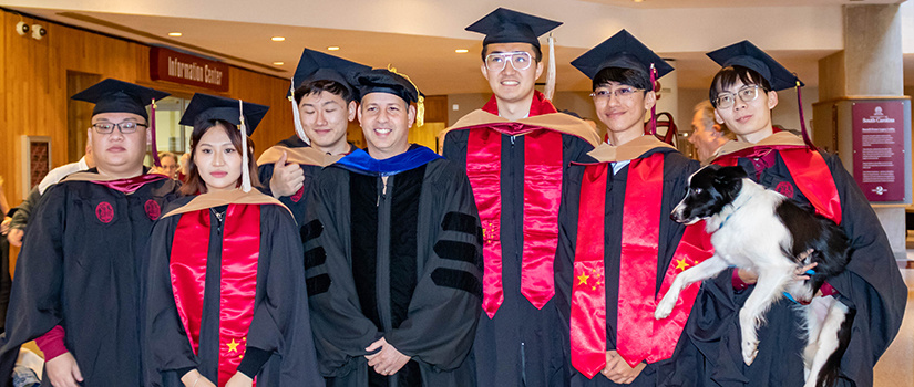 A group of international students pose for a photo with professor Stephen Shapiro at hooding and cording.