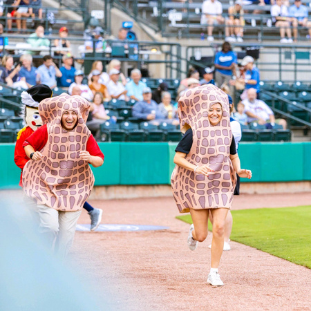 Too people running in peanut costumes on a baseball field