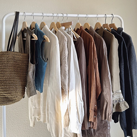Neutral-toned vintage clothing and a straw tote bag displayed on a white clothing rack.