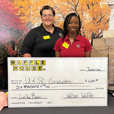 Two members of Waffle House pose with a large check written to UofSC graduates for $6,000.