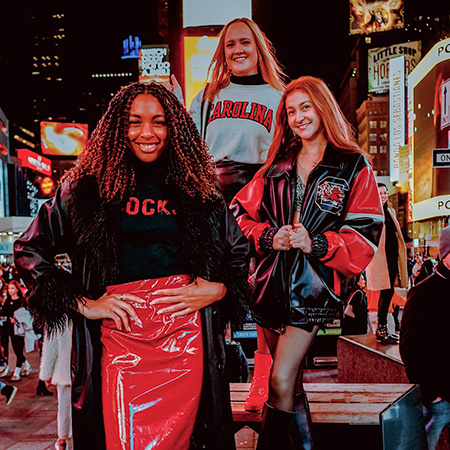 Three students pose for a photo in Times Square showing off their Gamecock clothing.